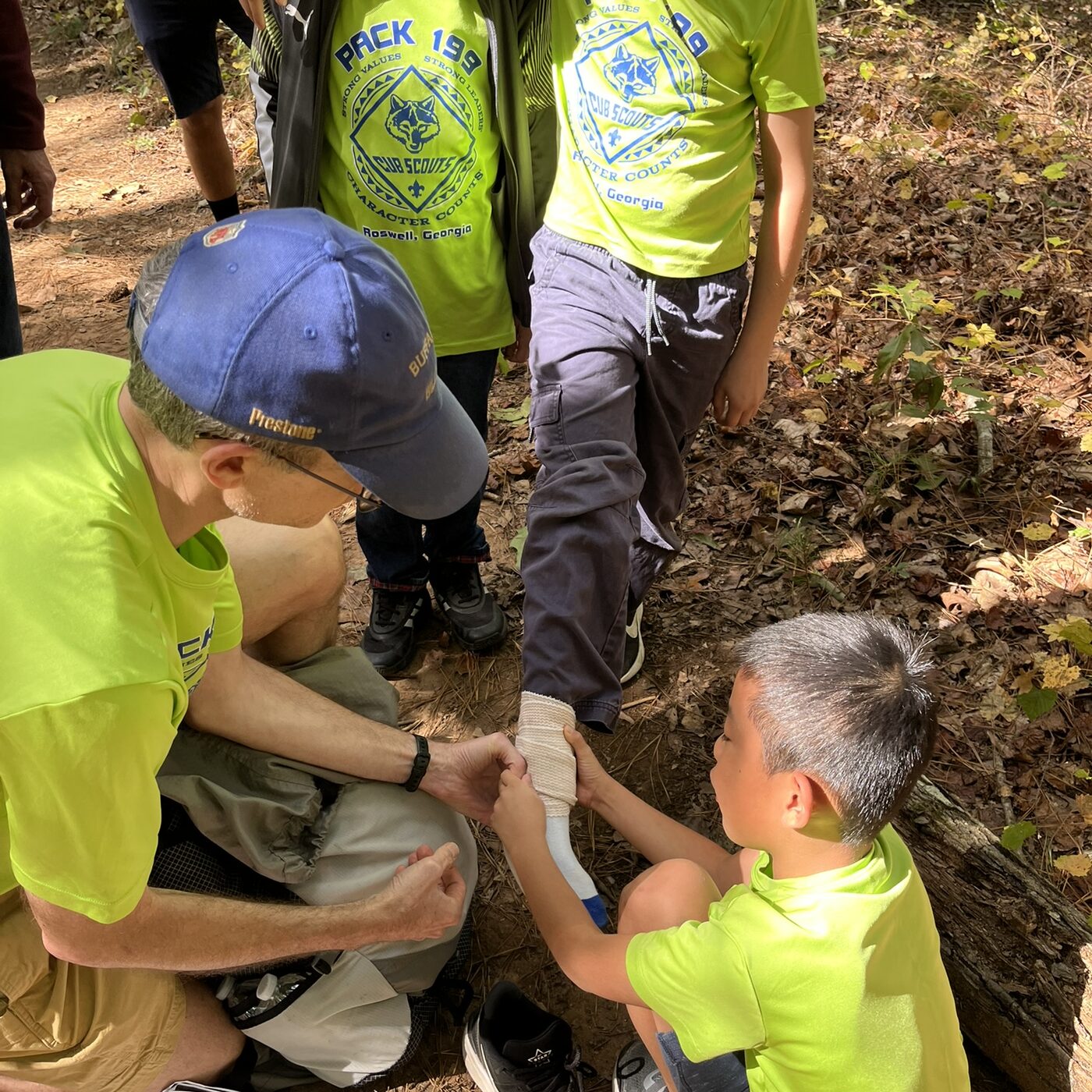 Pack 199 scouts practicing first-aid skills outdoors.
